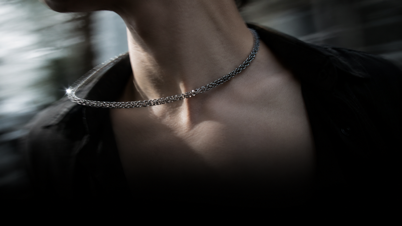 A stainless steel Byzantine chain caught mid-swing against a collarbone