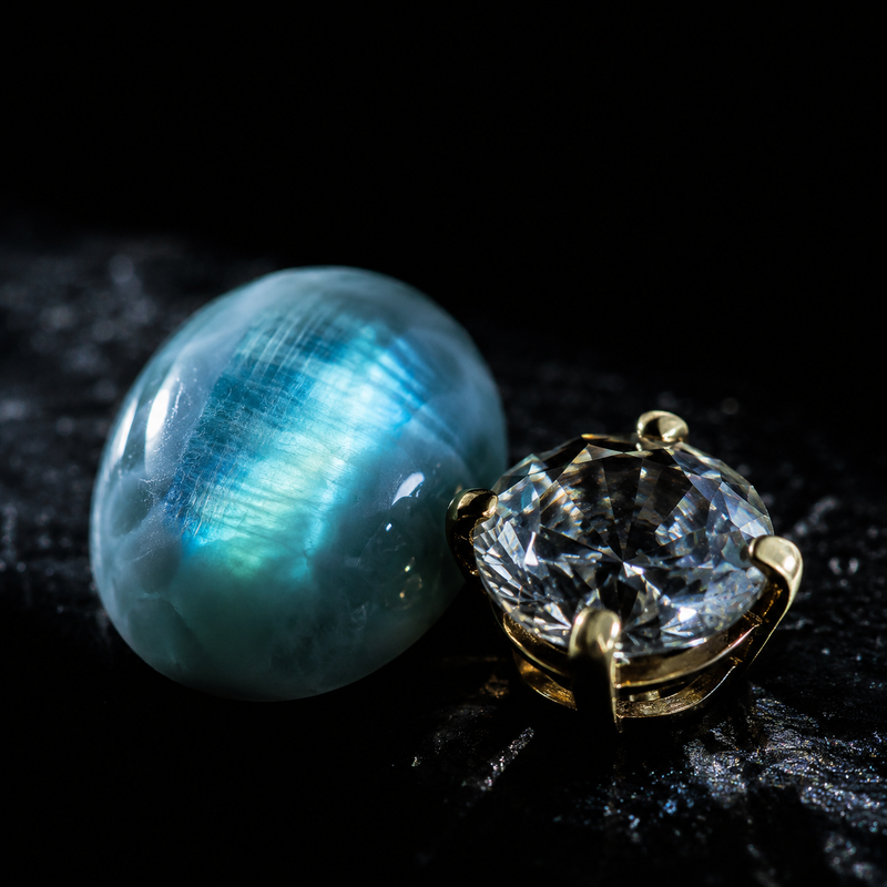A labradorite cabochon and a gold-set zirconia on a dark surface