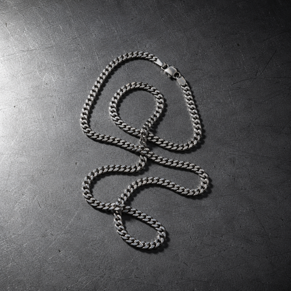 A steel Cuban link chain on a scratched steel surface