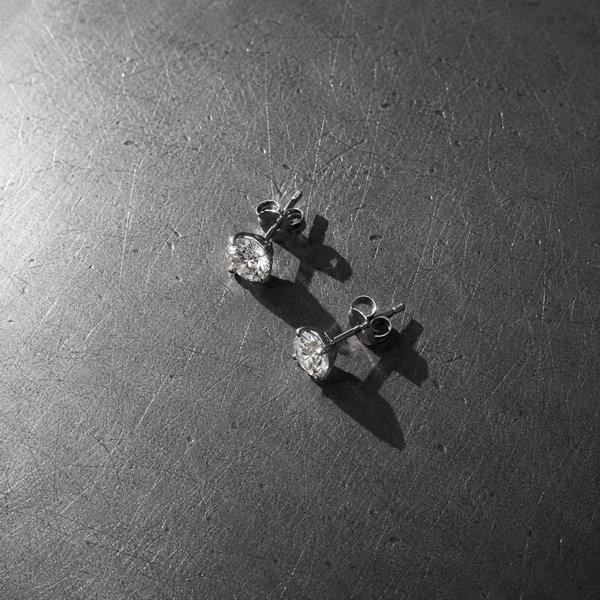 A pair of steel stud earrings on a scratched steel surface