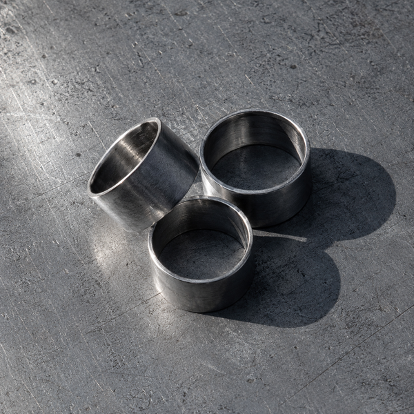 Three wide steel band rings on a scratched steel surface
